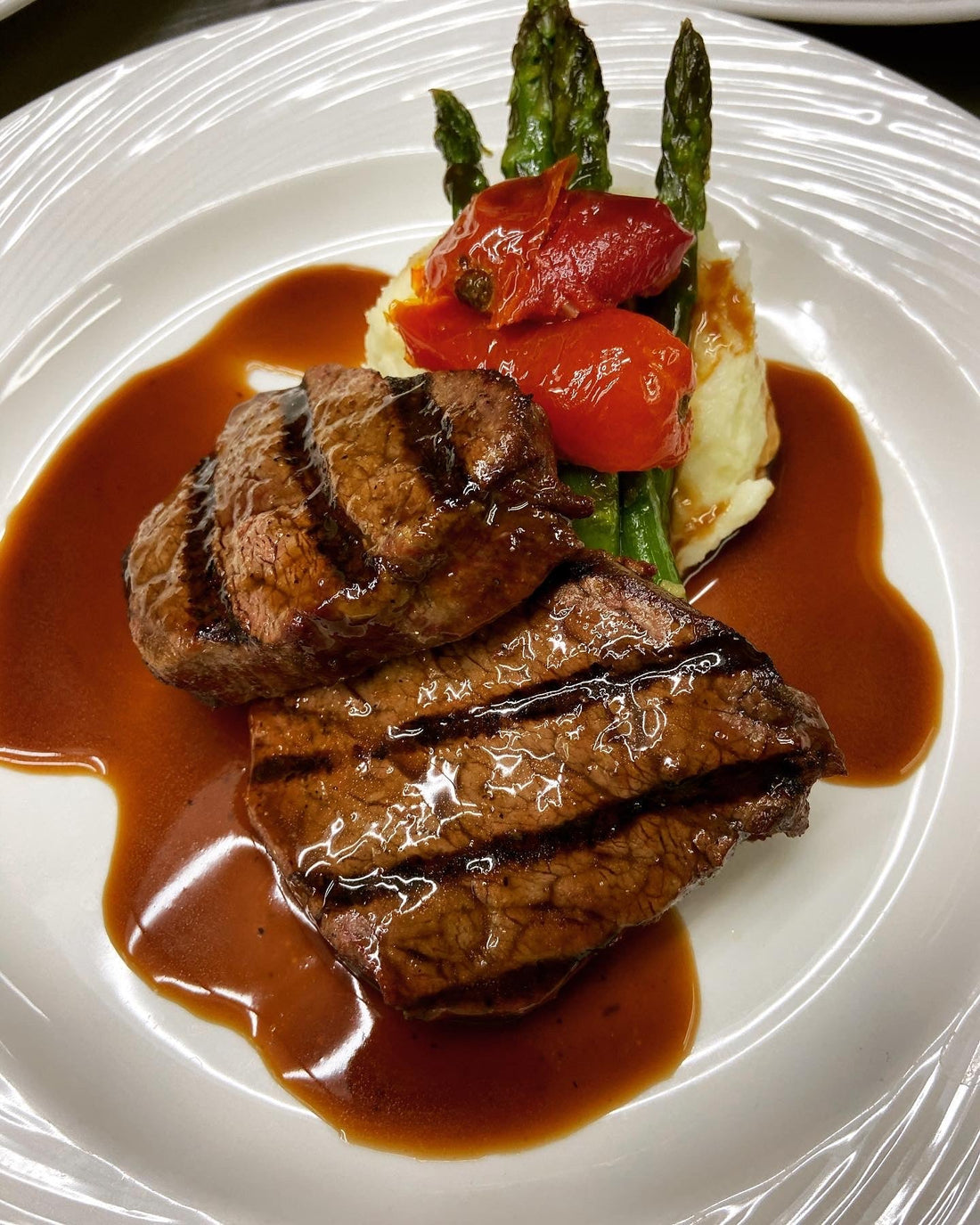 Grilled beef tenderloin medallions on a white plate with blue cheese mashed potatoes and fresh herbs