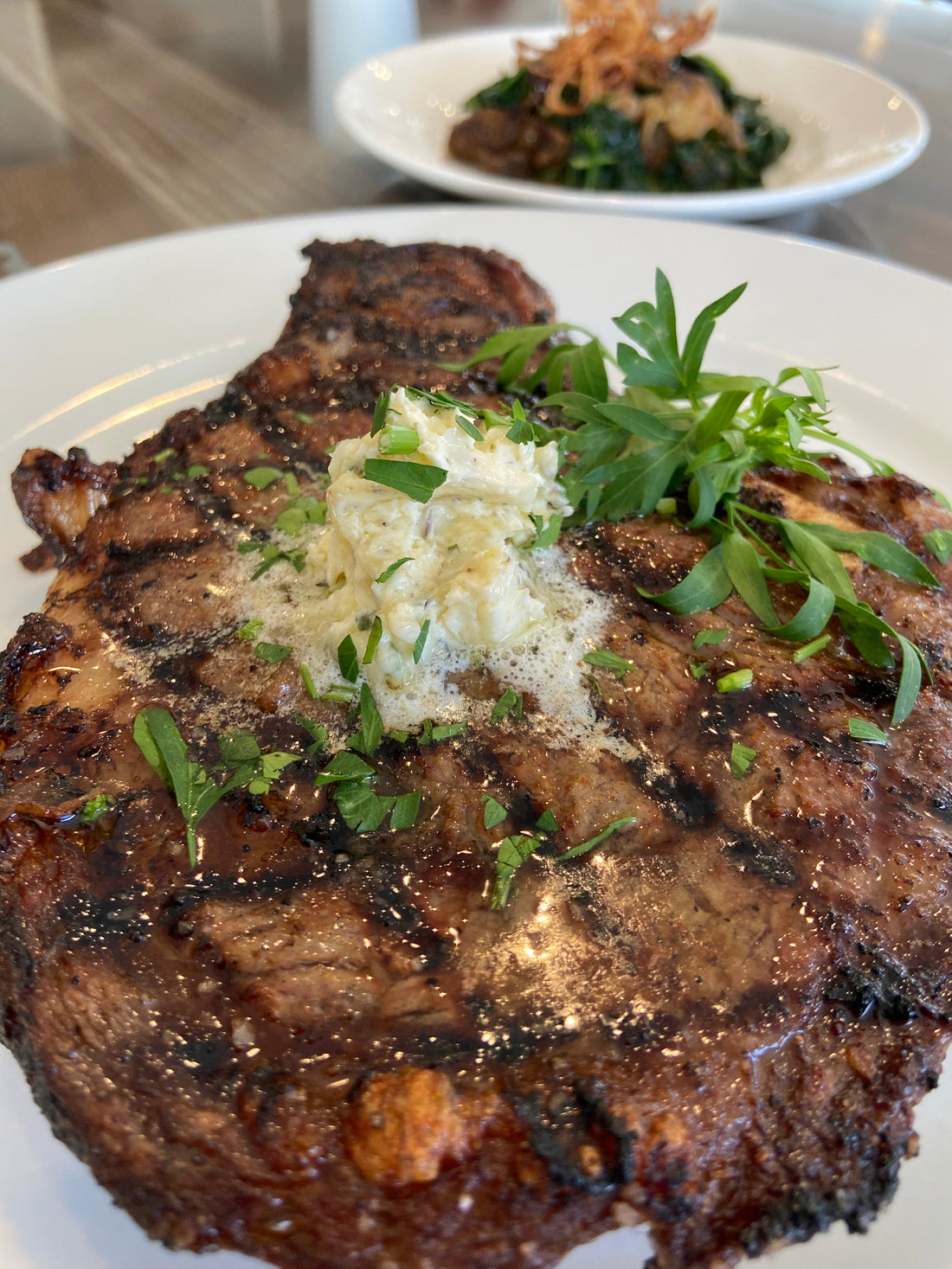 Grilled American Wagyu ribeye steak topped with herb compound butter, served with sautéed exotic mushrooms and crispy onions